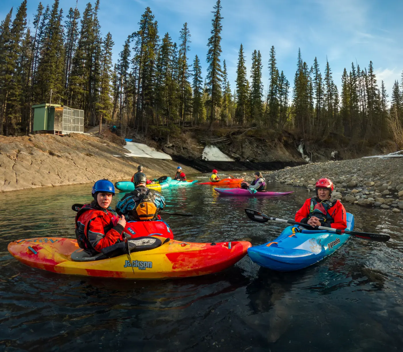 Airdrie Kayak Club paddlers gathered in an eddy with colourful whitewater kayaks