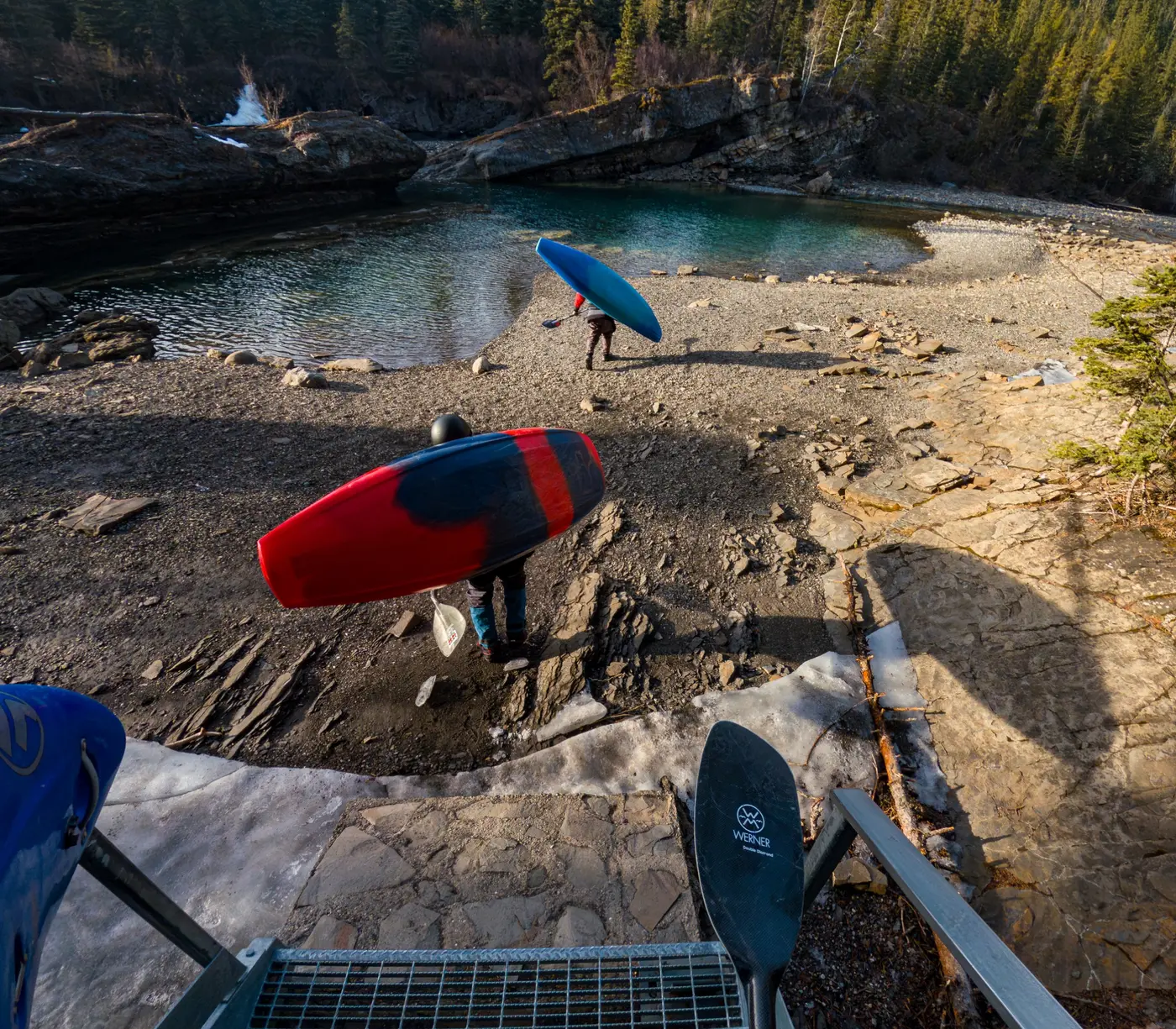 Two paddlers carrying kayaks toward the river